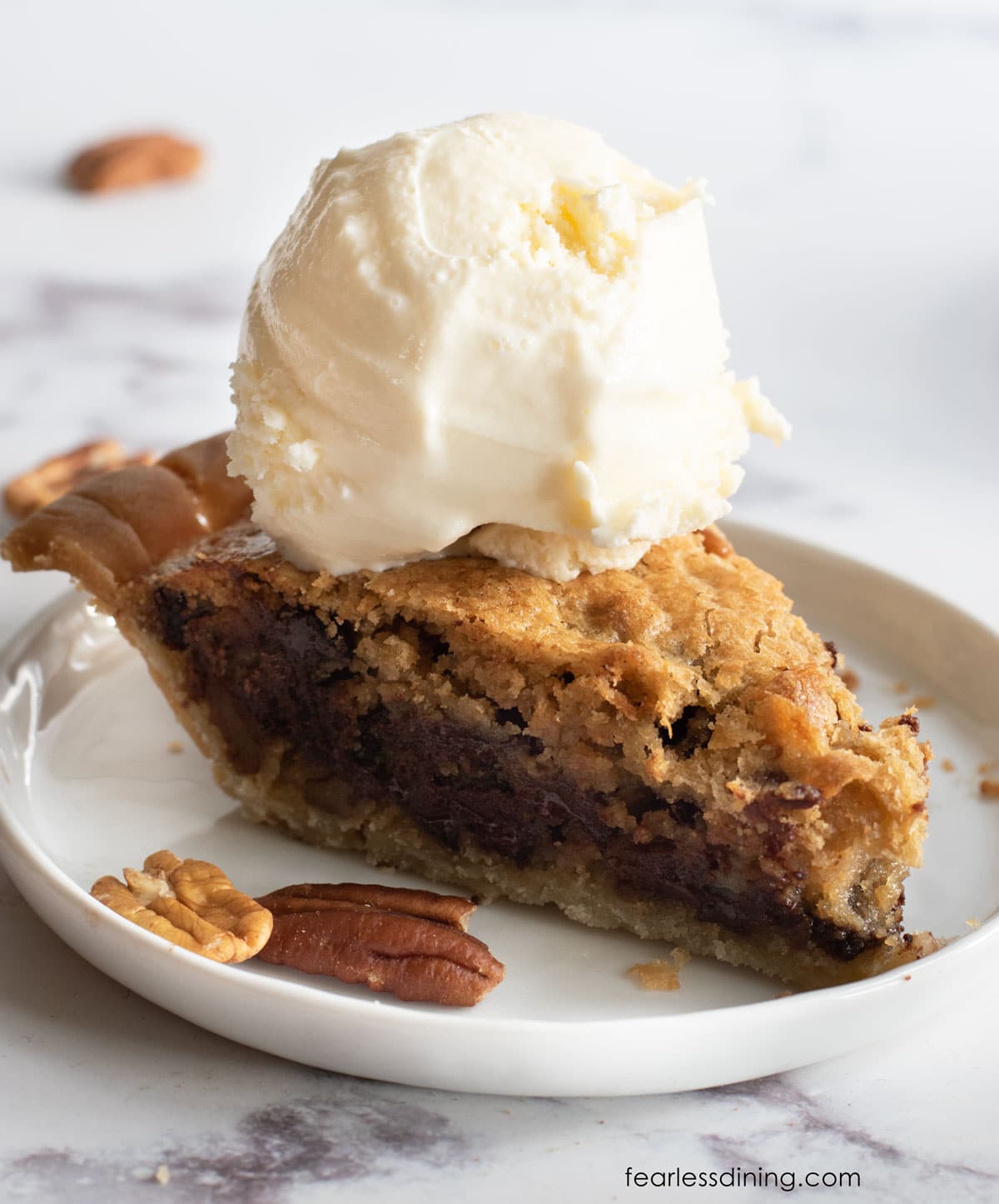 A slice of derby pie topped with a scoop of vanilla ice cream.