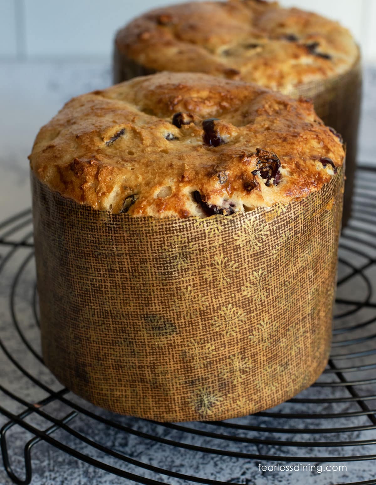 Two baked loaves of gluten free panettone bread on a rack.