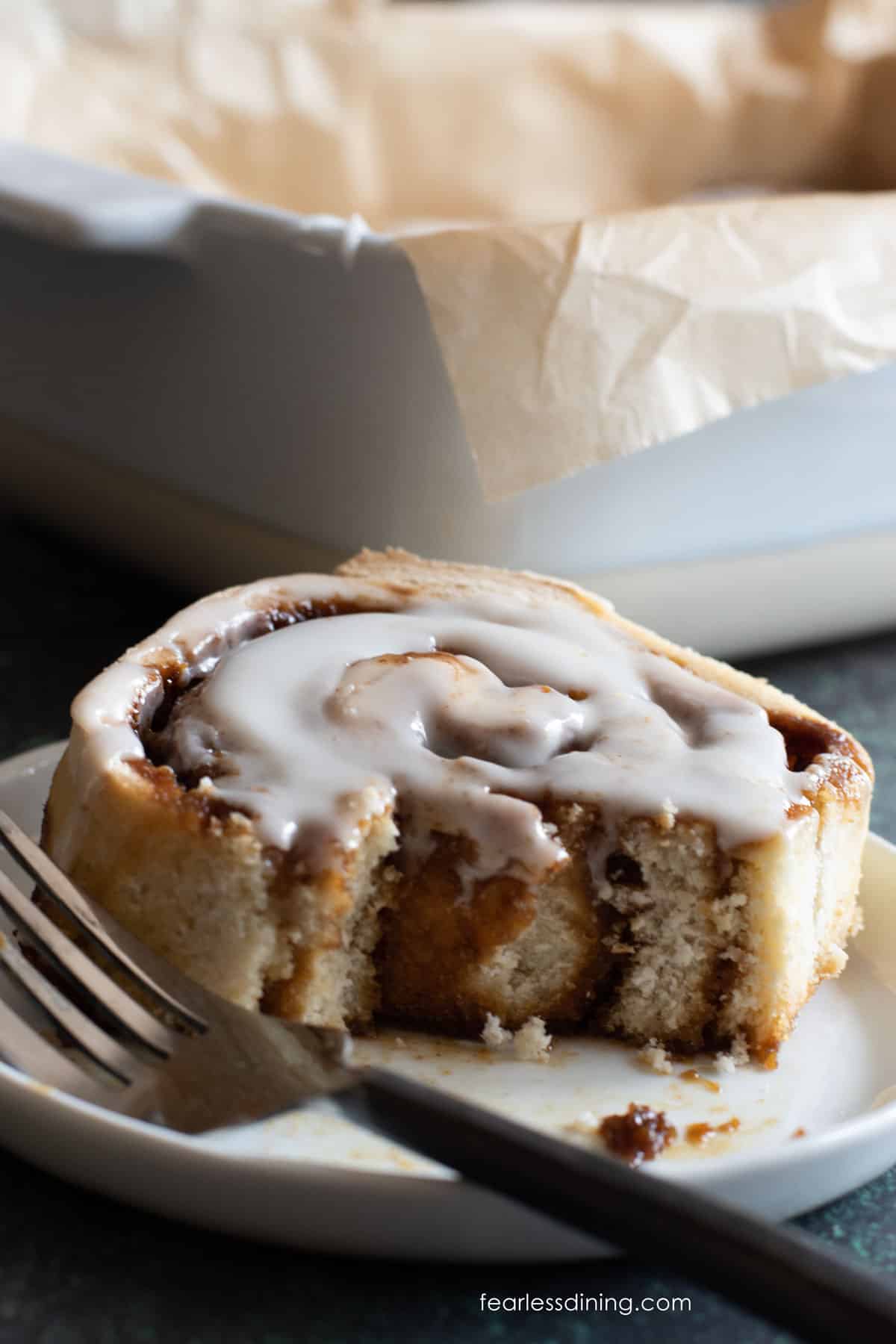 a gluten free gingerbread cinnamon roll on a small white plate. A bite is taken out.