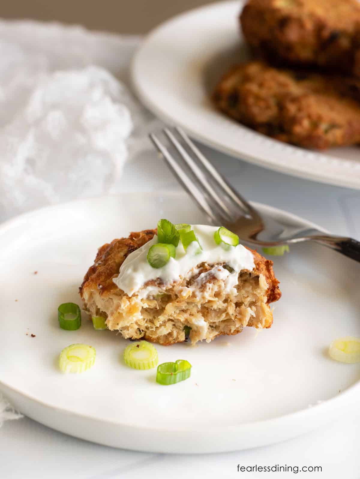 A partially eaten salmon cake on a plate with a fork next to it.