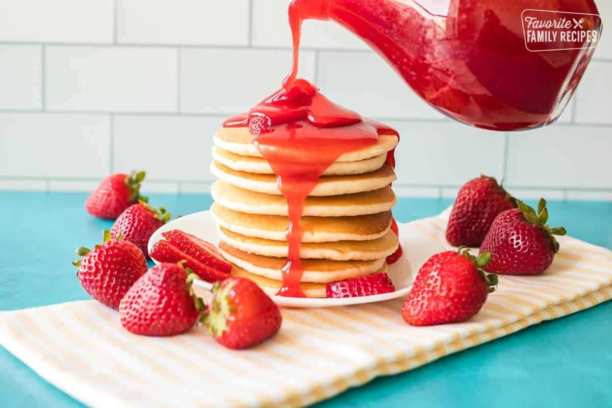 Pouring strawberry syrup over a stack of pancakes.