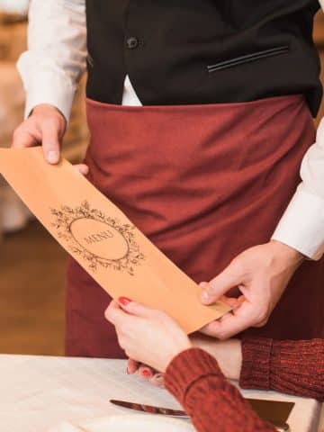 a waiter handing a menu to a customer in a restaurant.