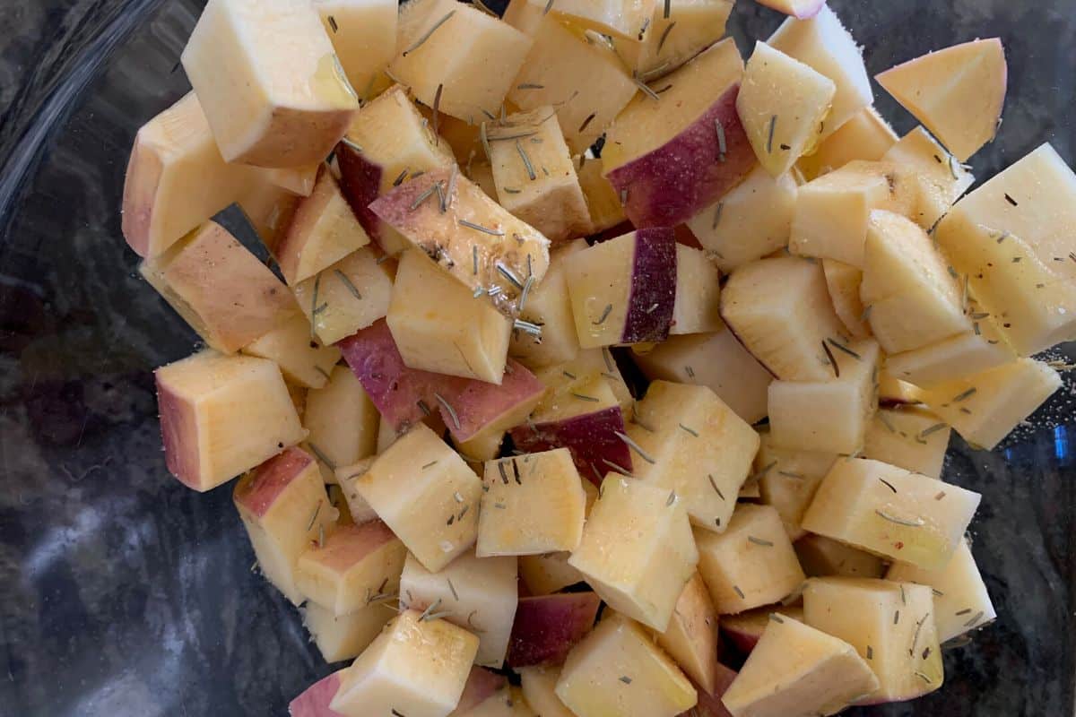 Cubed rutabagas with oil and dried herbs in a bowl.