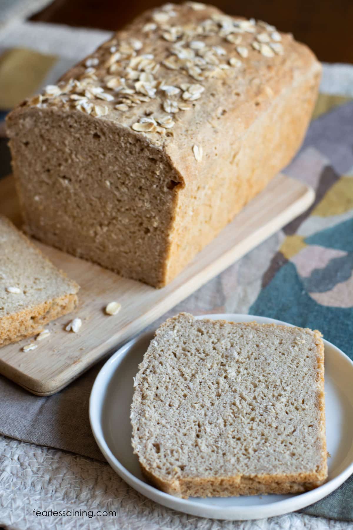 A slice of oat bread on a plate next to the sliced loaf.