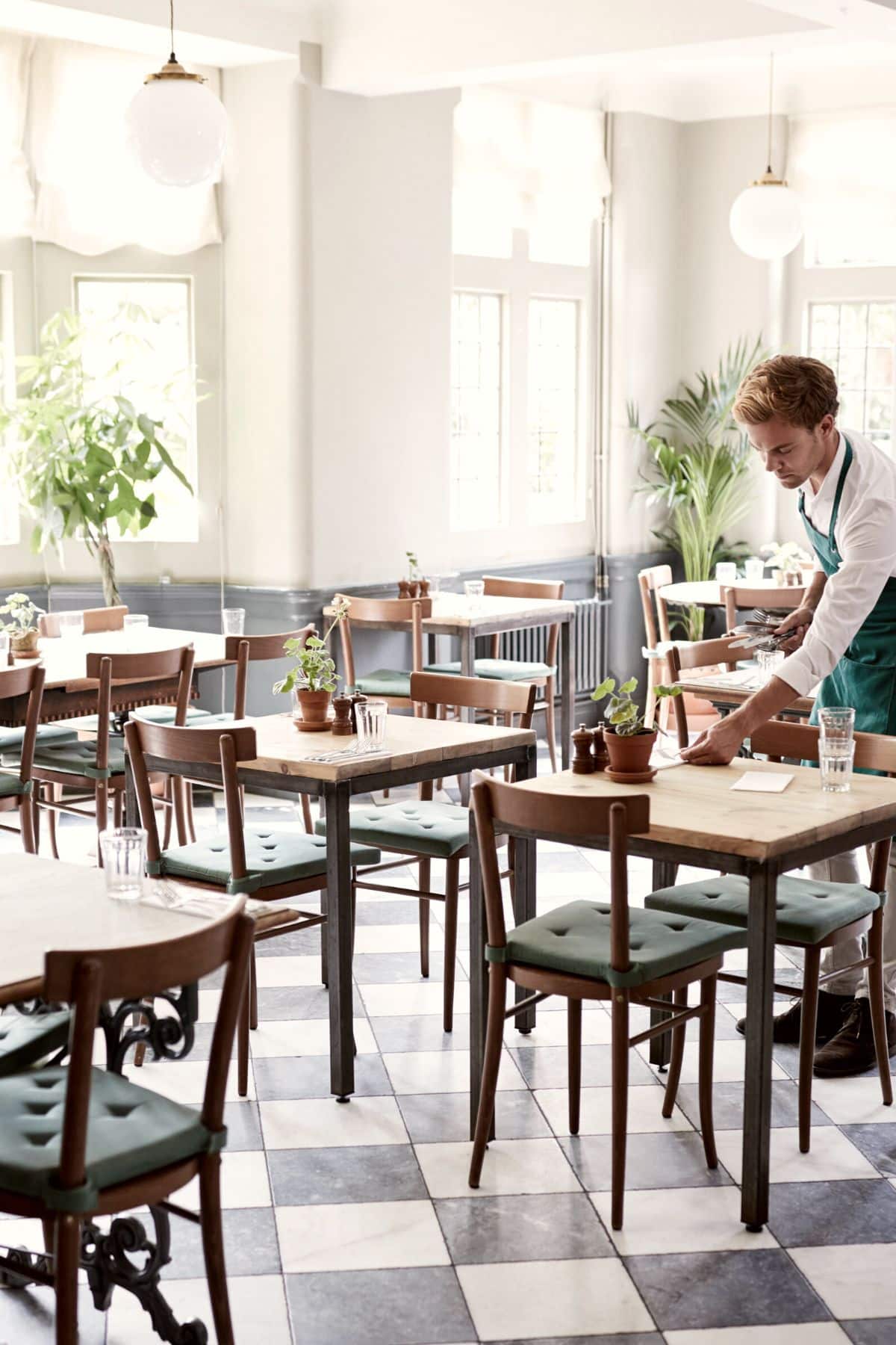 A photo of a waiter putting napkins on a table inside of a restaurant.