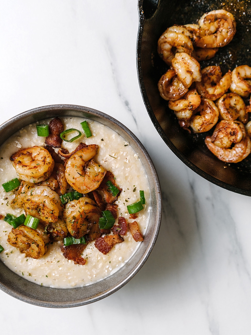A bowl of shrimp and grits next to a kale salad.