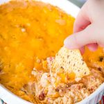 A photo of a hand dipping a chip into the jambalaya dip.