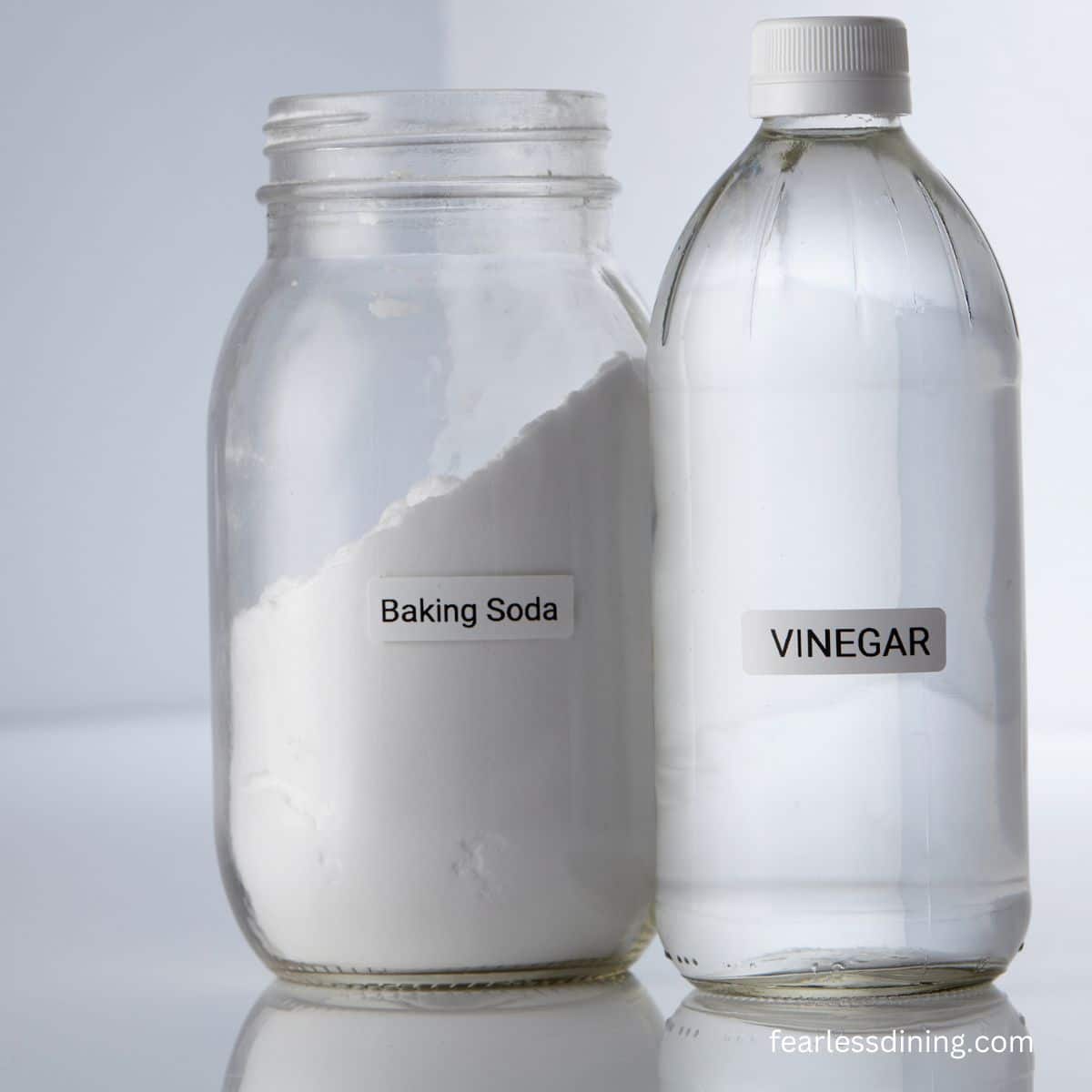 A jar of baking soda and a bottle of white vinegar next to each other on the counter.