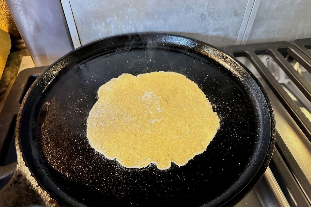 A corn tortilla cooking on a cast iron skillet.