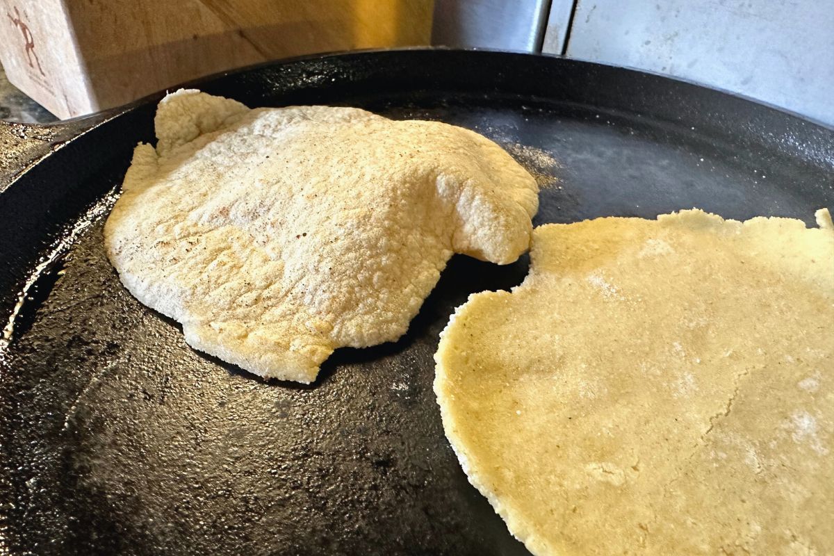 Two corn tortillas cooking on a skillet. One is puffing up with air.