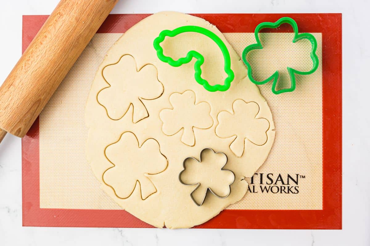 A photo of the cookie dough rolled out on a silicone mat with cookie cutters on the dough.