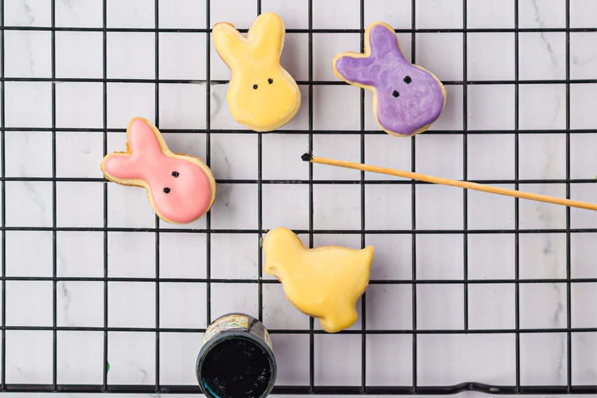 Mini bunny shaped cookies on a rack getting decorated.