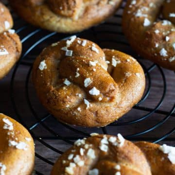 A bunch of gluten free soft pretzels cooling on a black wire rack.