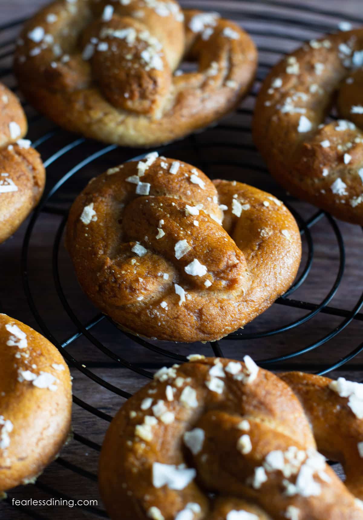 A bunch of gluten free soft pretzels cooling on a black wire rack.