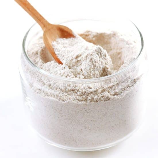 A glass jar filled with flour. A wooden scoop is in the jar.