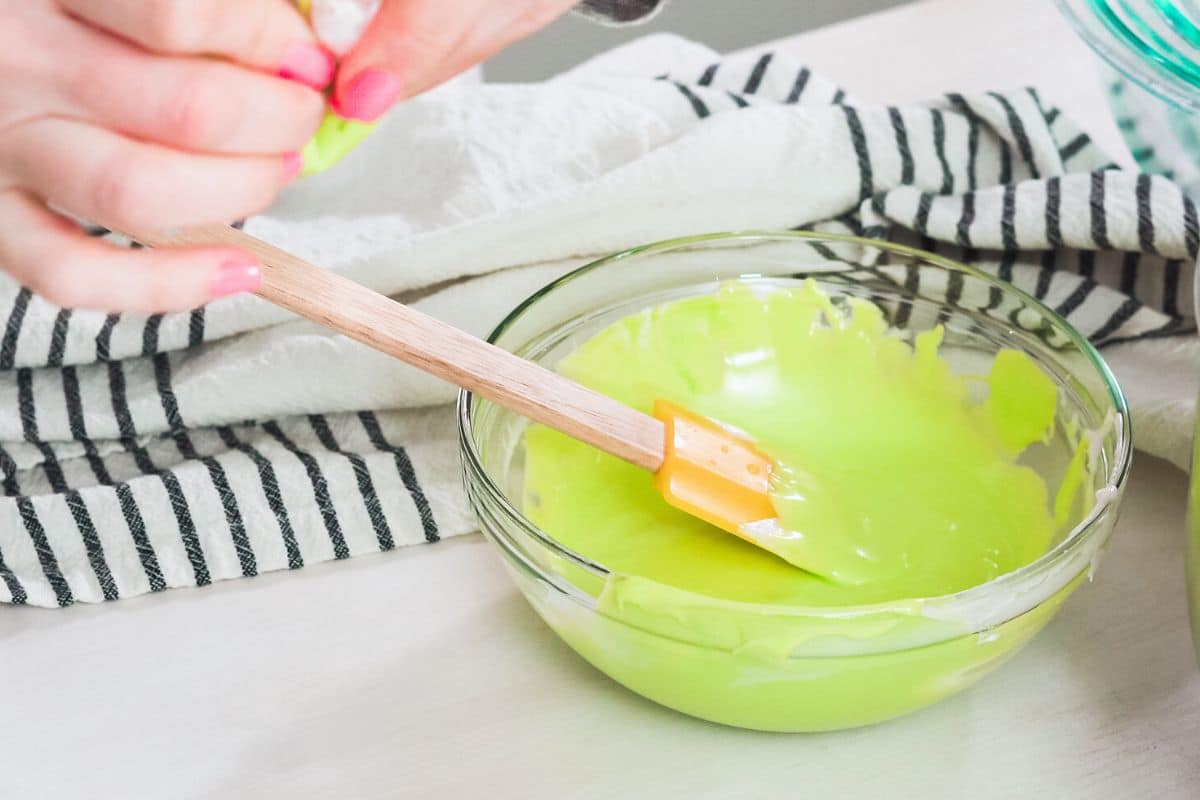 Mixing green royal icing in a bowl.