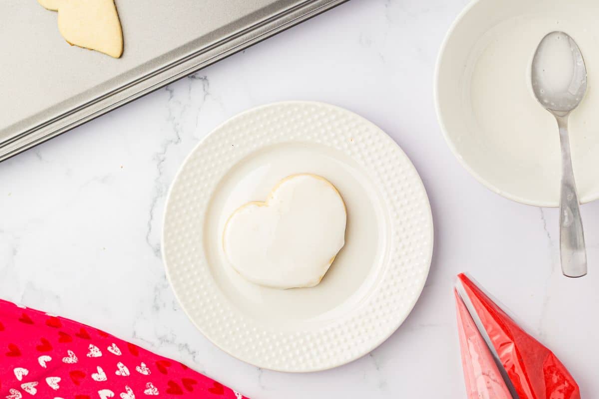 White icing coating the top of a heart shaped cookie.