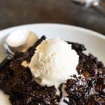 A plate with chocolate lava cake. It is topped with a scoop of vanilla ice cream.