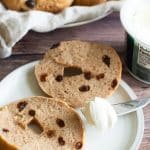 A gluten free cinnamon raisin bagel sliced in half on a small white plate.