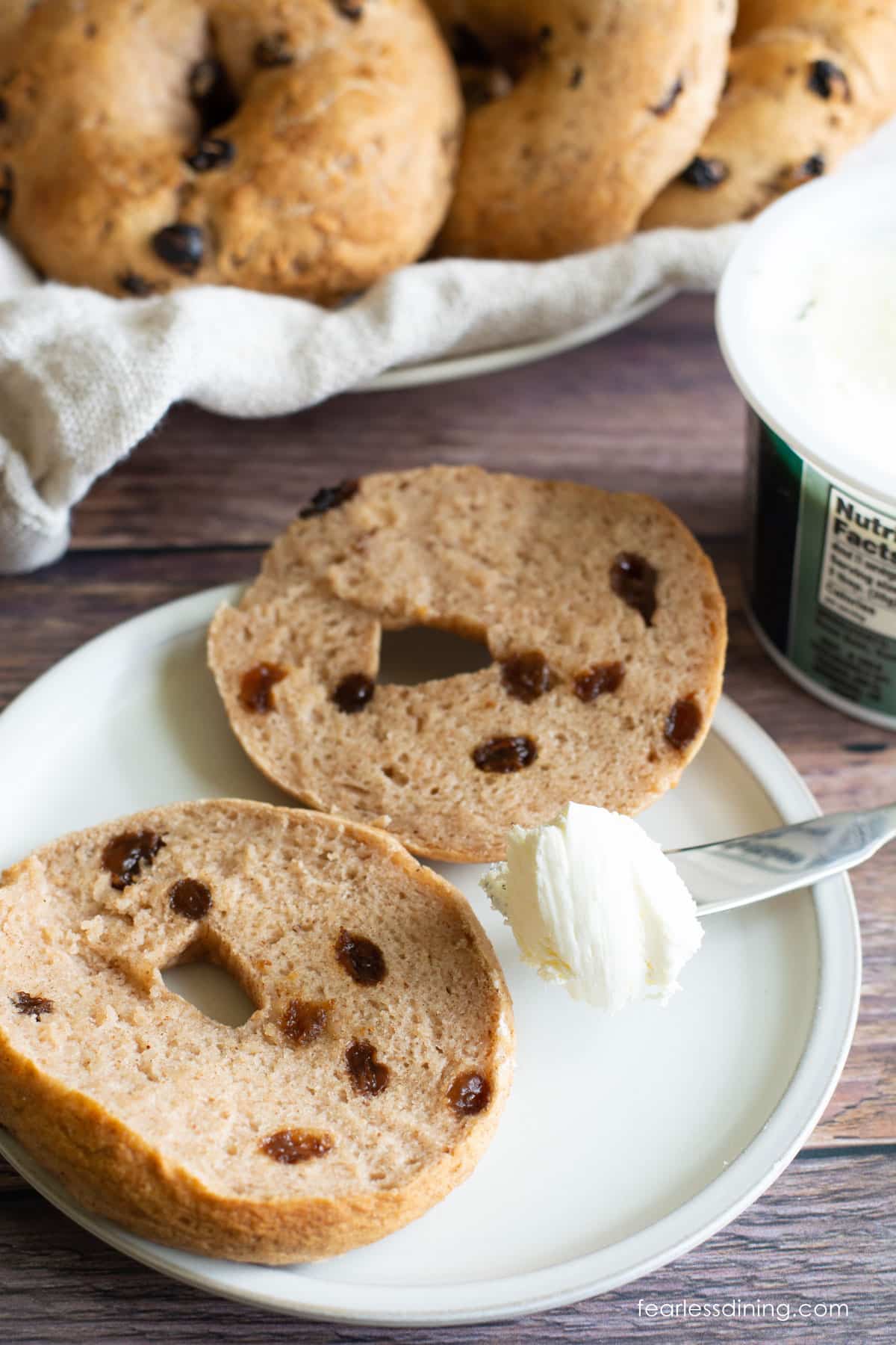 A gluten free cinnamon raisin bagel sliced in half on a small white plate.