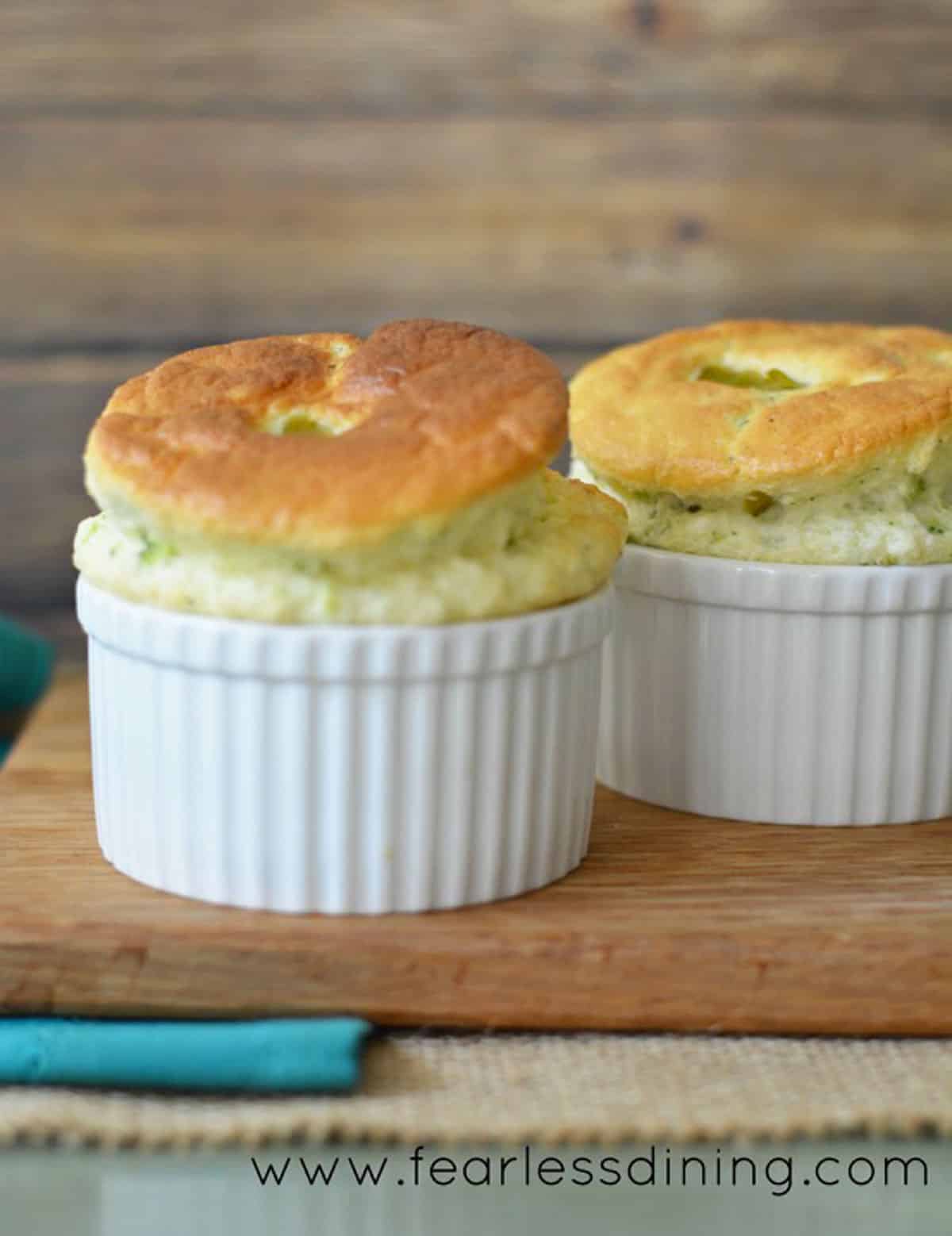 Two gluten free souffles in white ramekins on a wooden board.