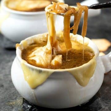 A spoon lifting up caramelized onions and cheese from a bowl of French onion soup.