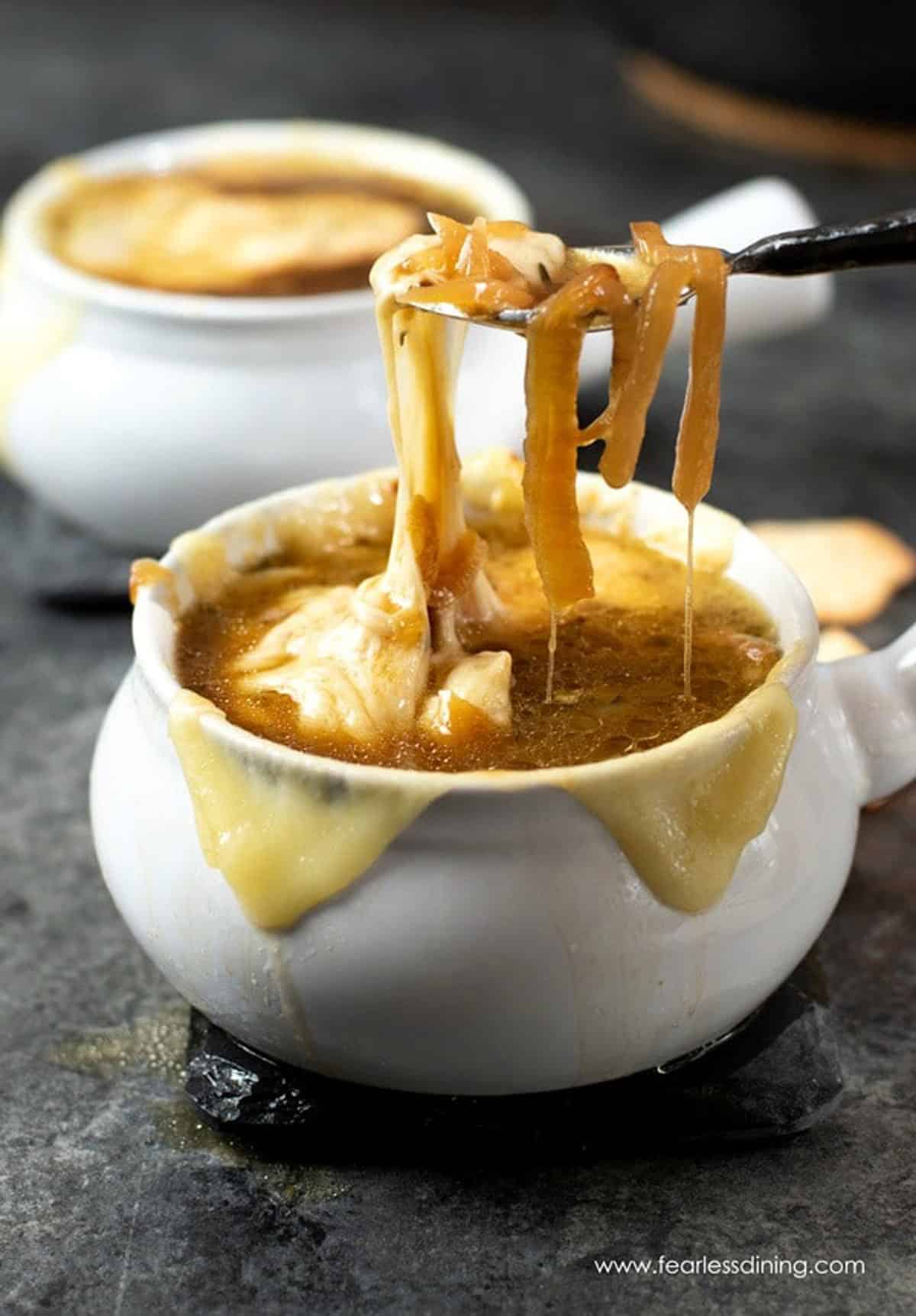 A spoon lifting up caramelized onions and cheese from a bowl of French onion soup.