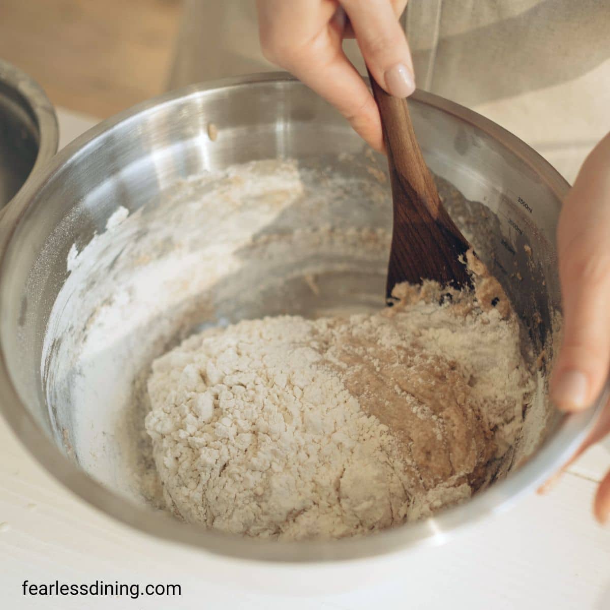 Mixing bread dough ingredients in a big silver bowl.