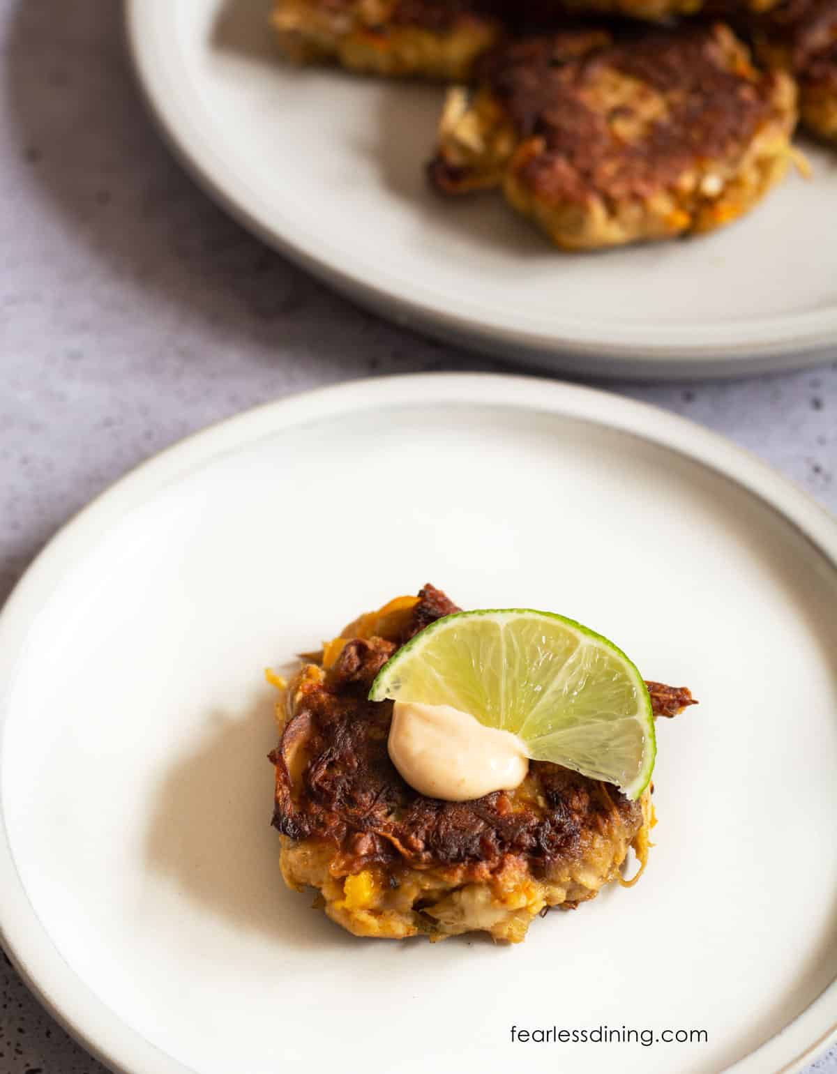 The top view of crab cakes on a plate. It is garnished with sauce and a lime wedge.