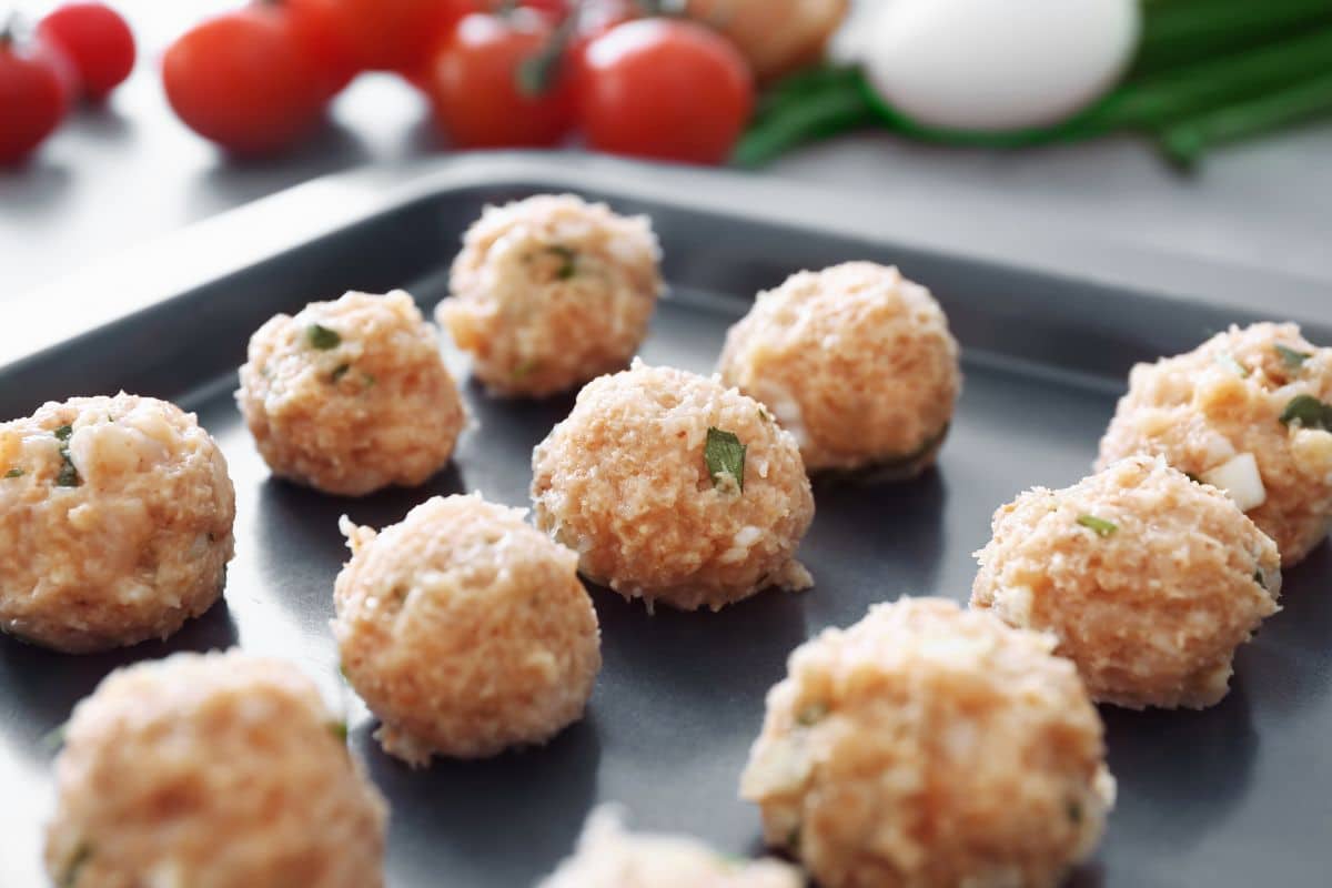 Rows of meatballs on a tray ready to be dropped into the cooking sauce.