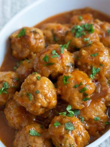 A white serving dish filled with sweet and sour meatballs.