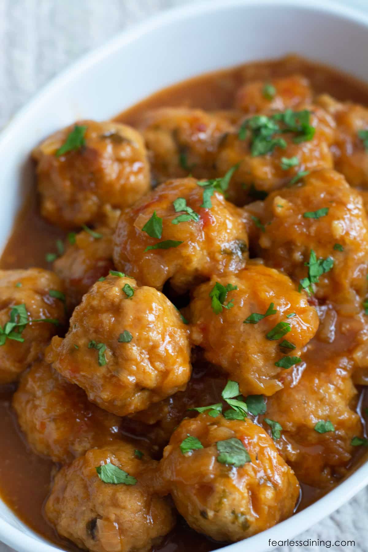 A white serving dish filled with sweet and sour meatballs.