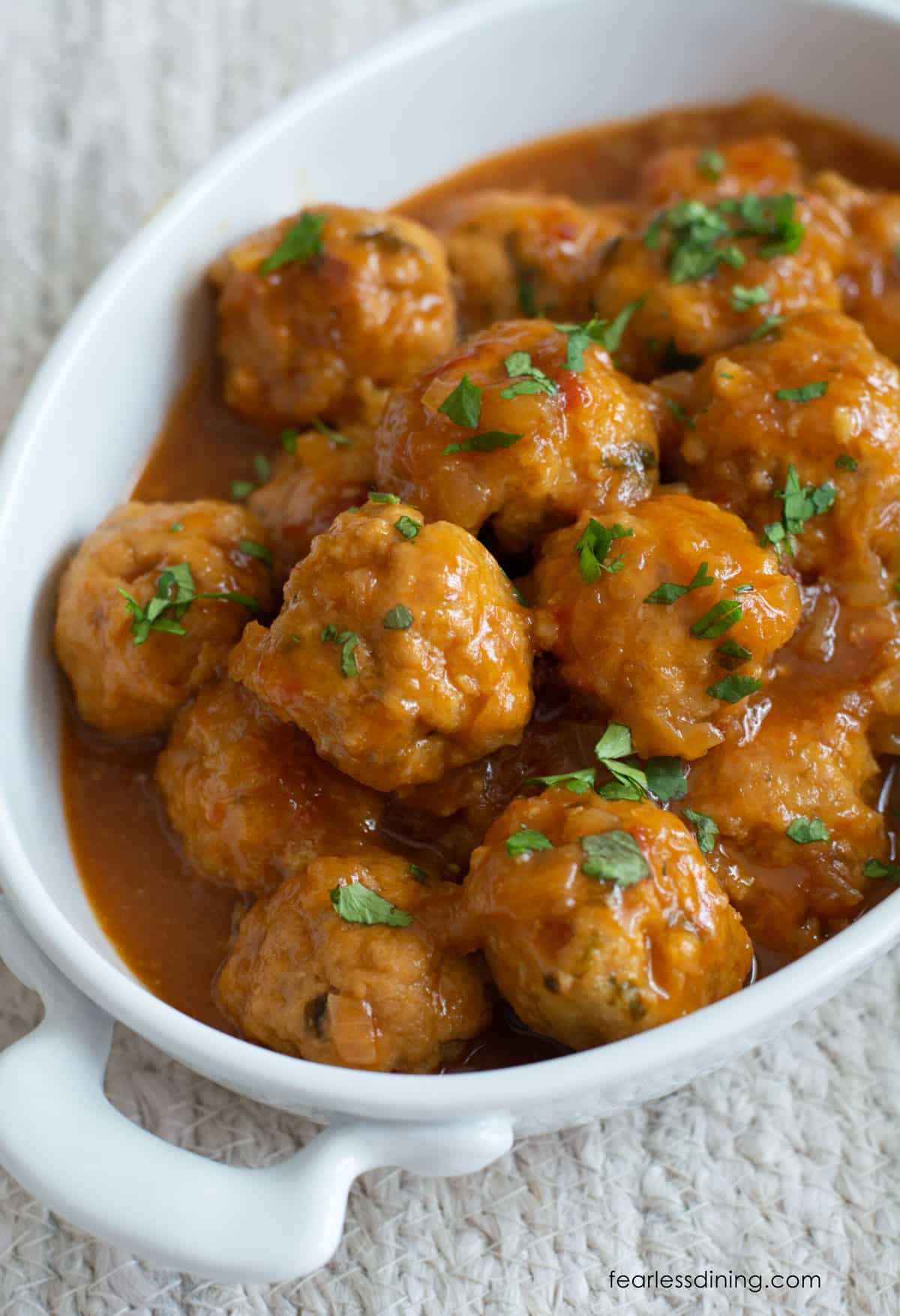 A close up of the sweet and sour meatballs in a white serving dish.