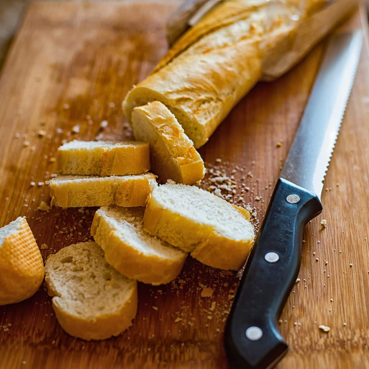 Slicing a gluten free baguette on a wooden cutting board.