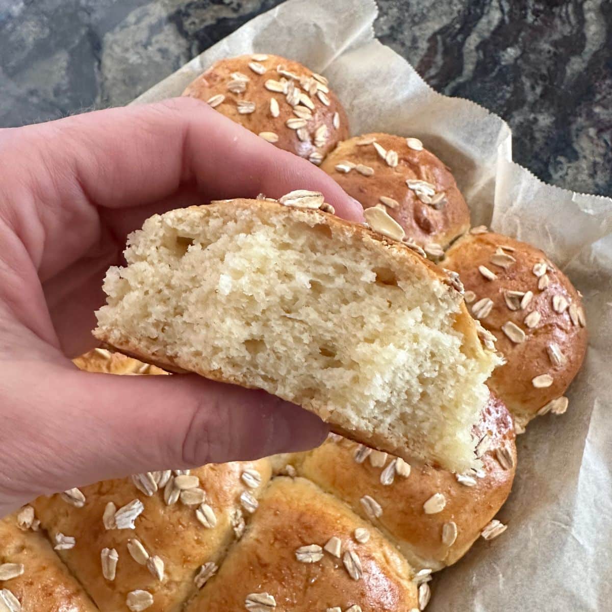 Holding up a honey roll with a bite taken out so you can see the inside of the roll.