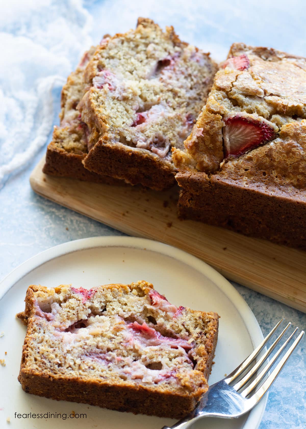 A slice of strawberry banana bread on a plate next to the sliced loaf.