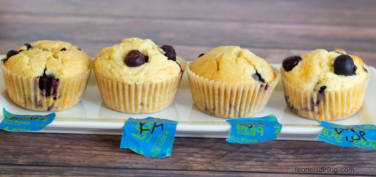 All four gluten free blueberry muffins side by side on a rectangular plate.