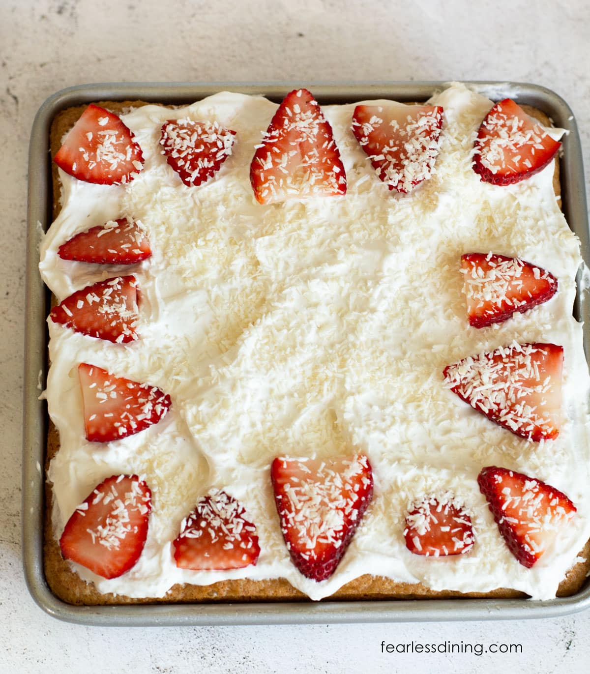 The top of a tres leches cake with strawberry slices and shredded coconut.