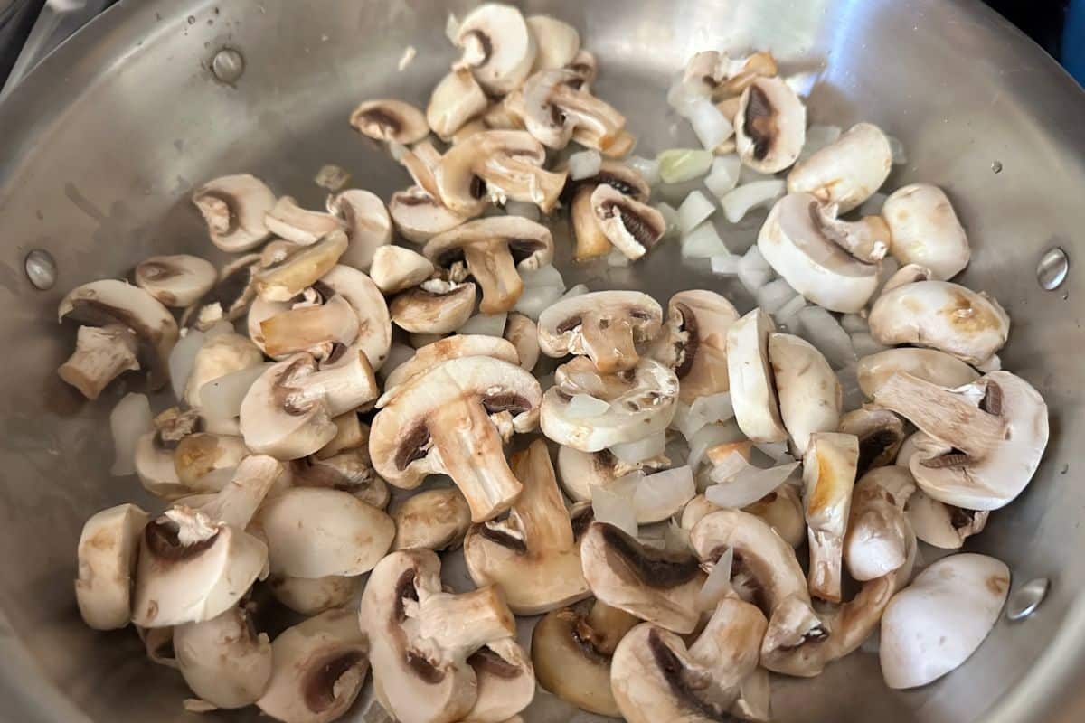 Sliced ushrooms and onions cooking in a large pan.
