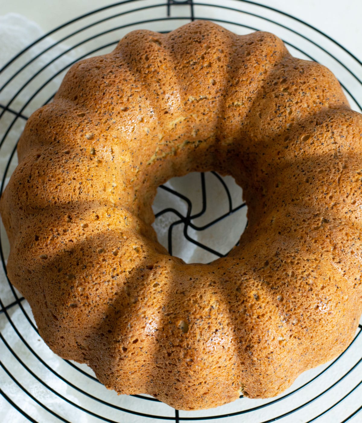 An orange bundt cake on a black wire cooling rack.