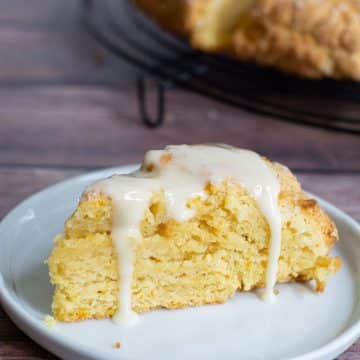 A gluten free orange scone on a plate. The scone has orange icing dripping down over the sides of the scone.