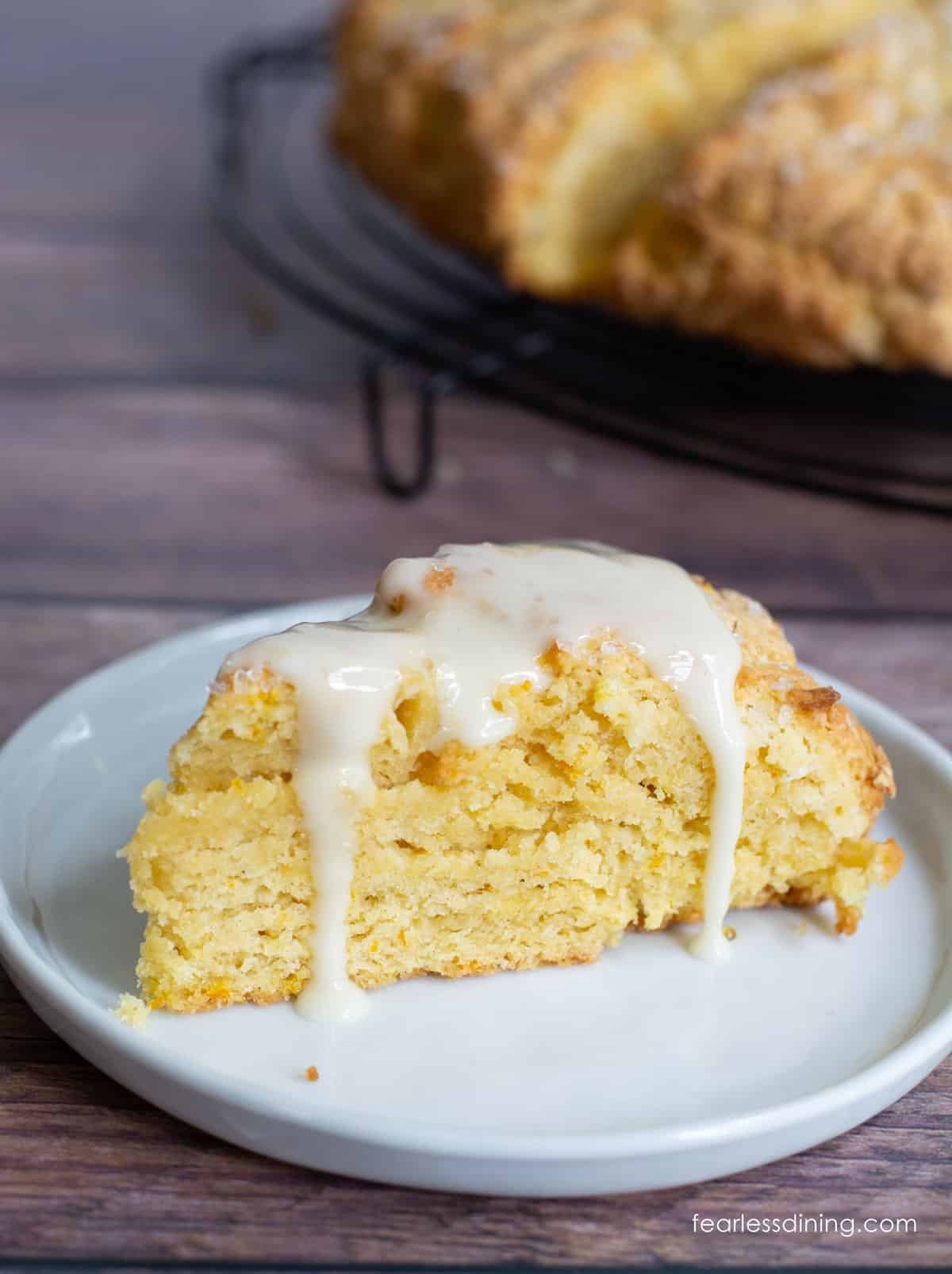 A gluten free orange scone on a plate. The scone has orange icing dripping down over the sides of the scone.