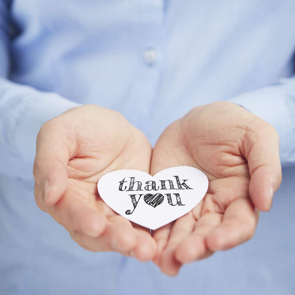 Two hands holding a handwritten thank you written on a paper heart.