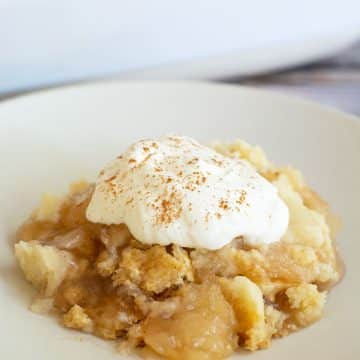 A serving of gluten free apple dump cake topped with whipped cream.