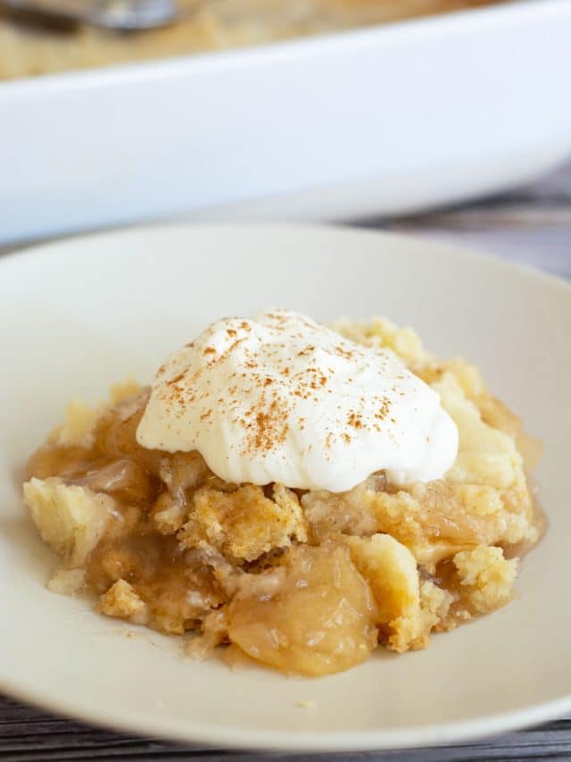 A serving of gluten free apple dump cake topped with whipped cream.