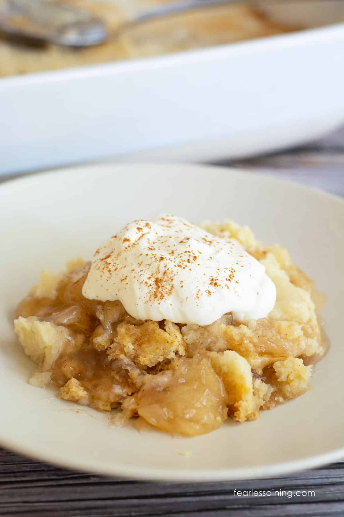 A serving of gluten free apple dump cake topped with whipped cream.