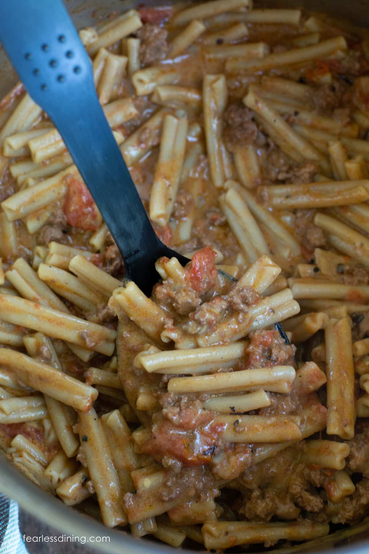 A black serving spoon in a pot of cheeseburger pasta.