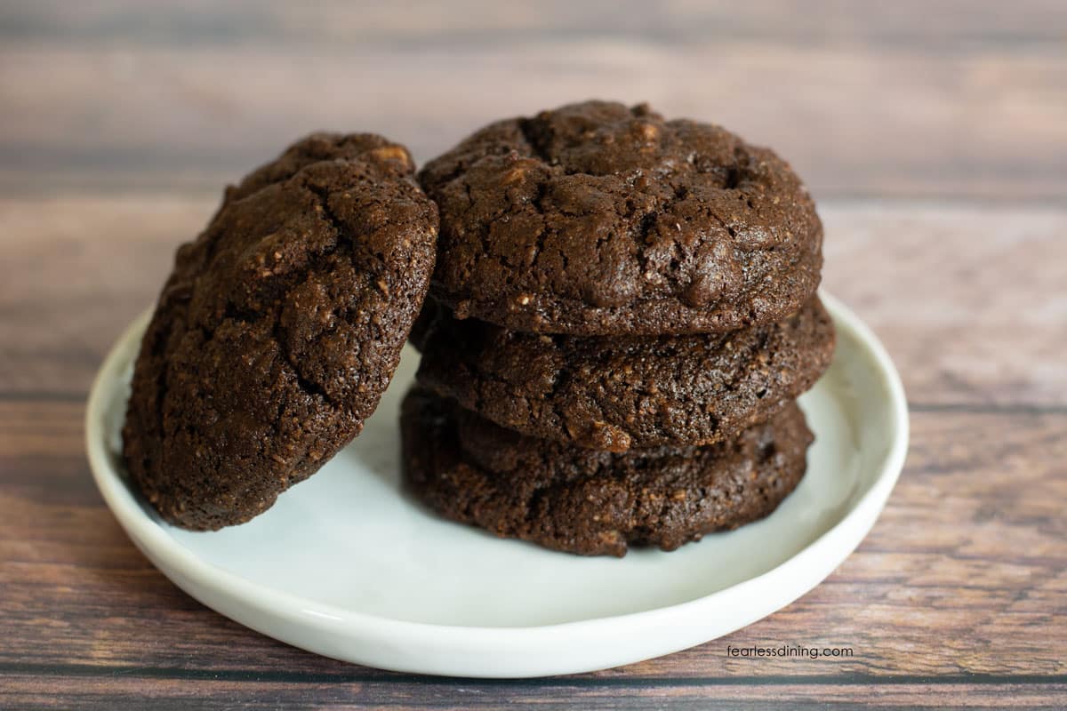 A stack of three cookies on a small white plate. Another cookie is leaning on the stack.