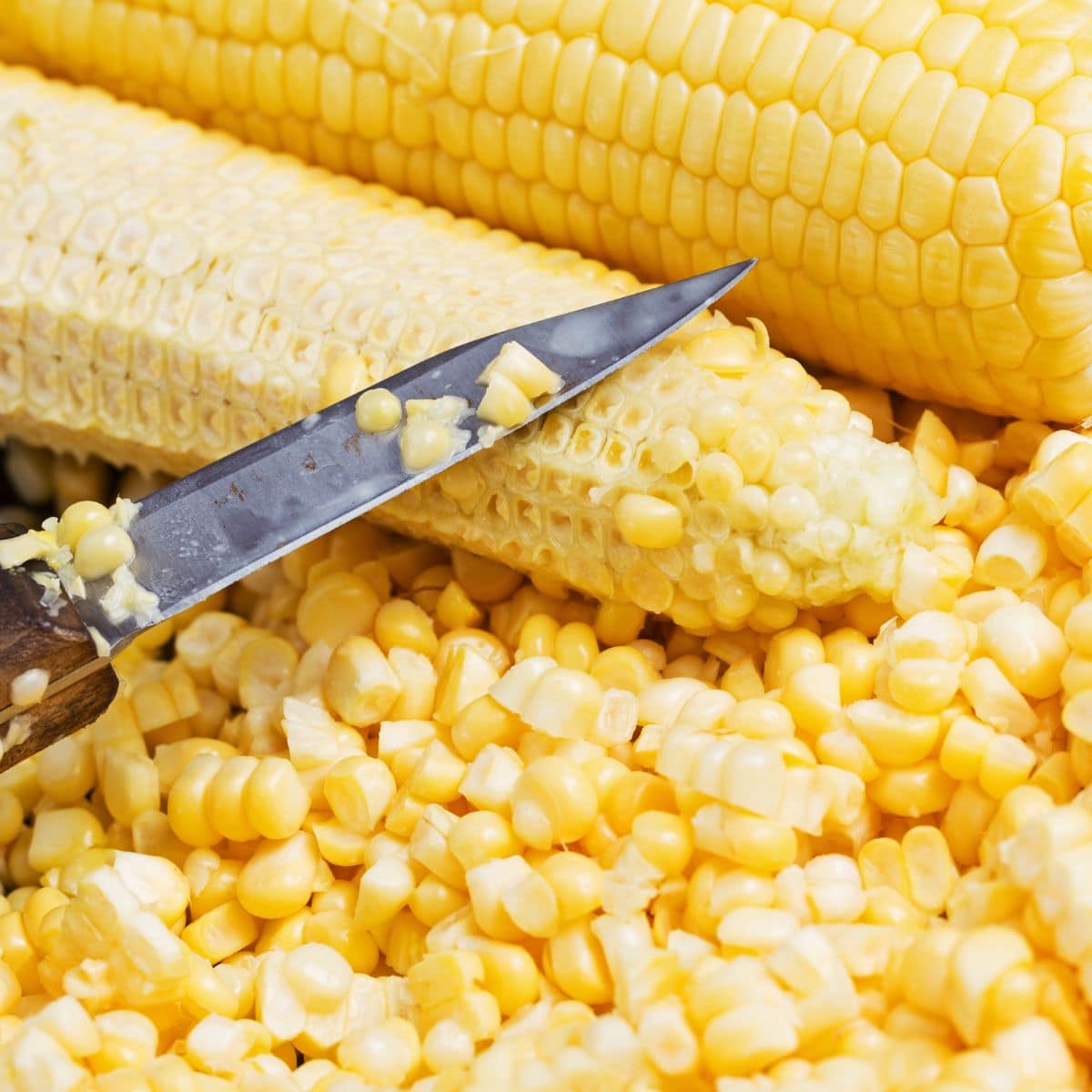 Using a sharp knife to remove corn kernels from the cob.