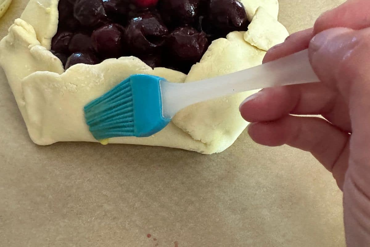 Brushing an egg wash over the galette dough.